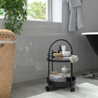 Black FRÖSJÖN bathroom trolley with towels, bottles, and a brush by bathtub and window.