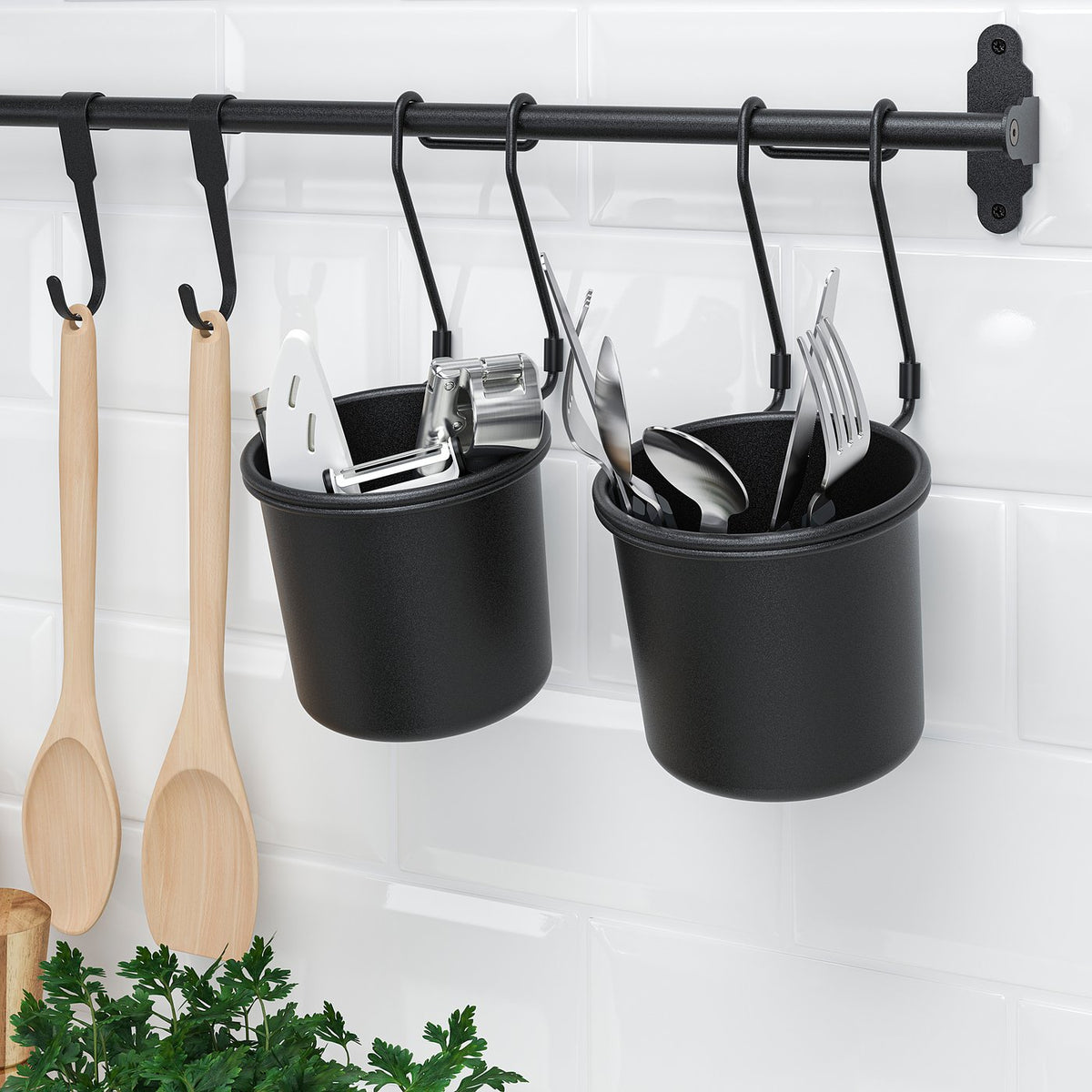 Black hanging utensil pots with kitchen tools, mounted on a rail with hooks, against white tiled wall.