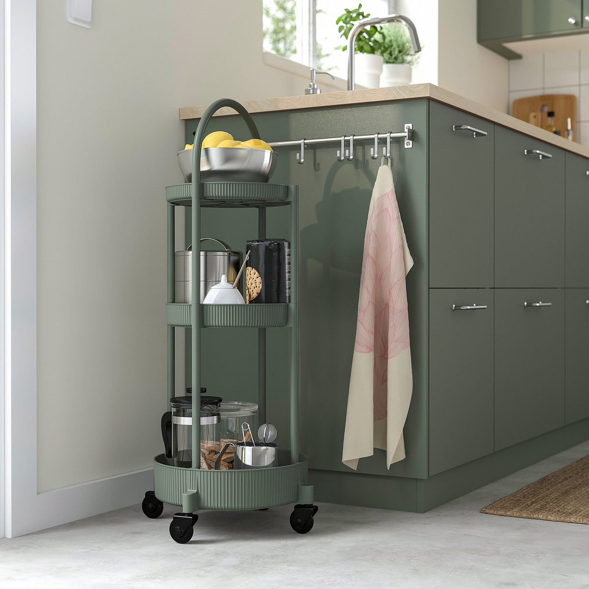 Grey-green JUTTERSBO trolley with kitchen items, beside cabinets.