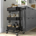 Black three-tiered RÅSKOG trolley in kitchen, holding jars and food, on wheels, compact size.
